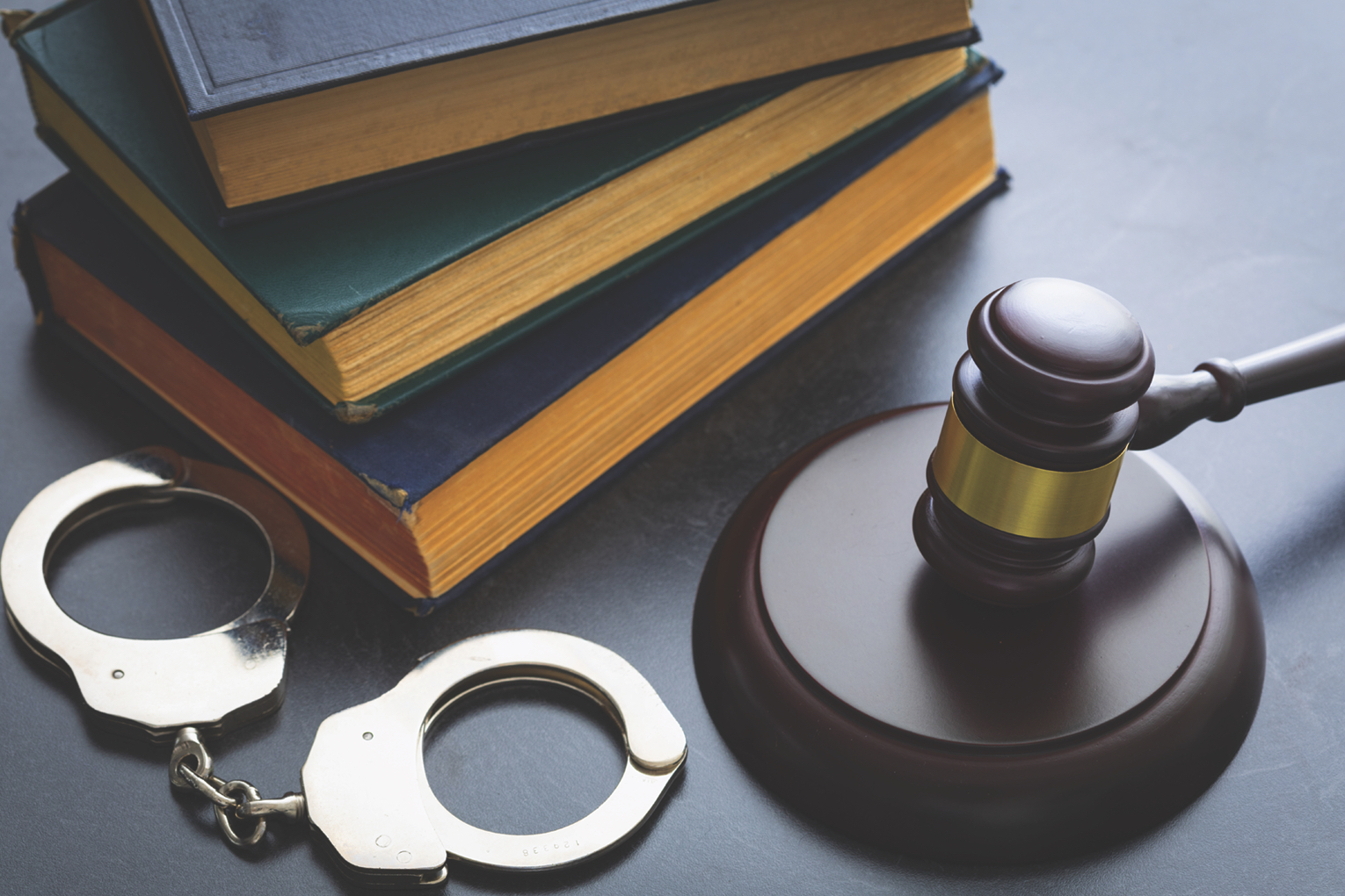 A stock image showing a pair of handcuffs next to a judicial gavel surrounded by important looking books